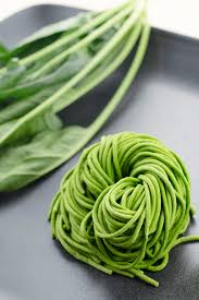 A bowl of green spinach noodles made with real spinach, served with vegetables and herbs